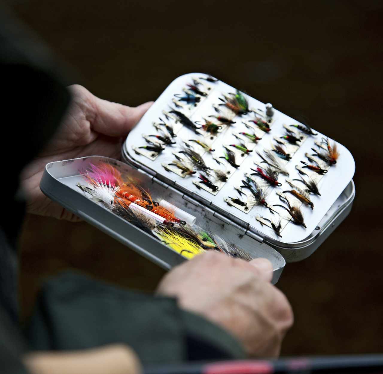 hands holding open fly box with assortment of fly fishing flies